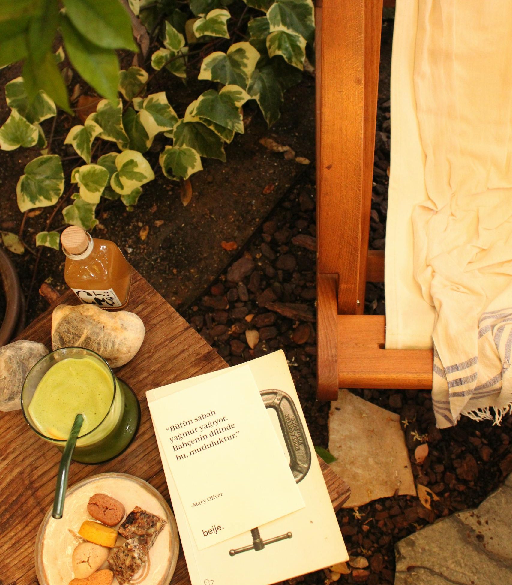 Warm outdoor scene with a book, snacks, drink, and chair amidst greenery.